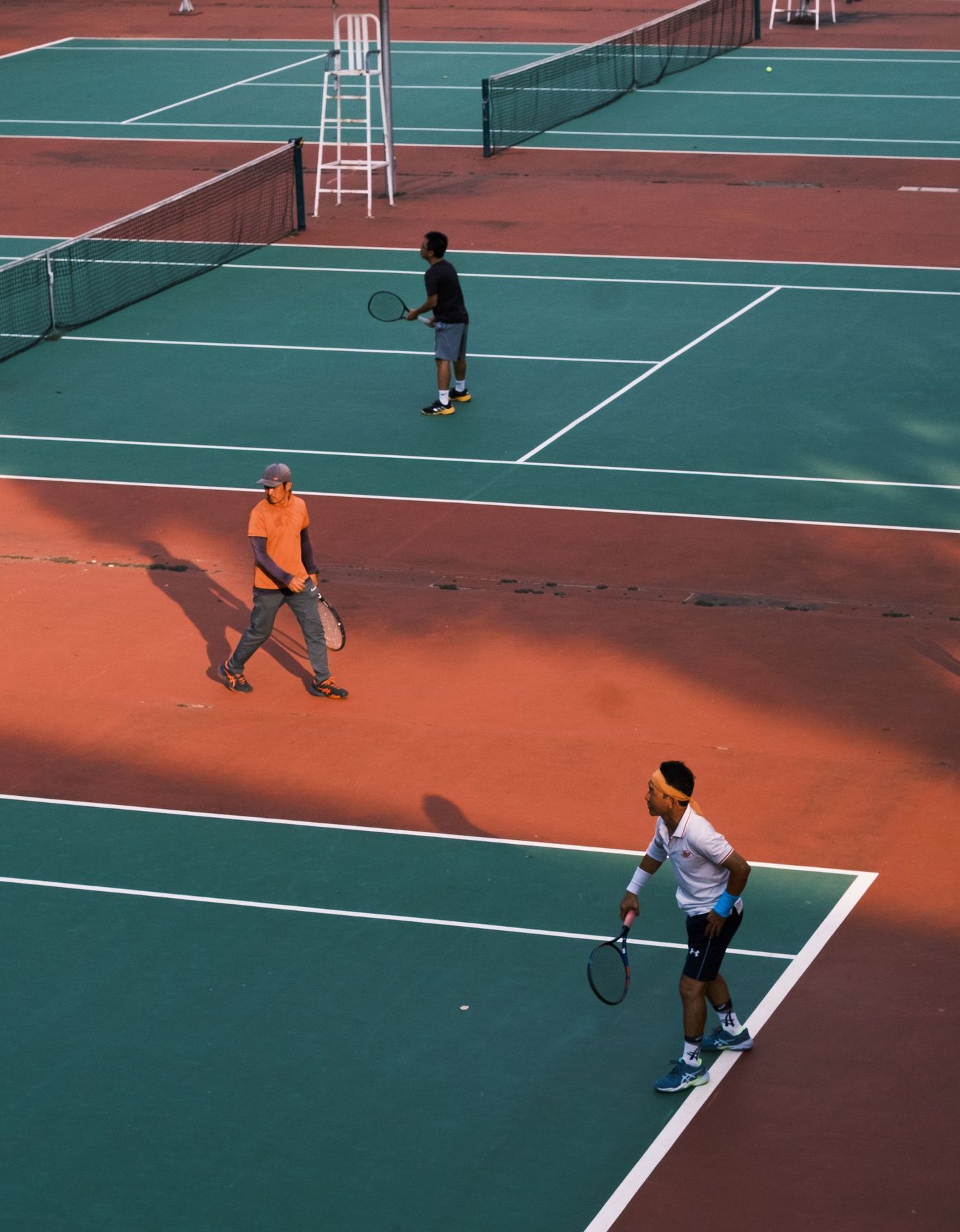 Three adults playing tennis on outdoor courts