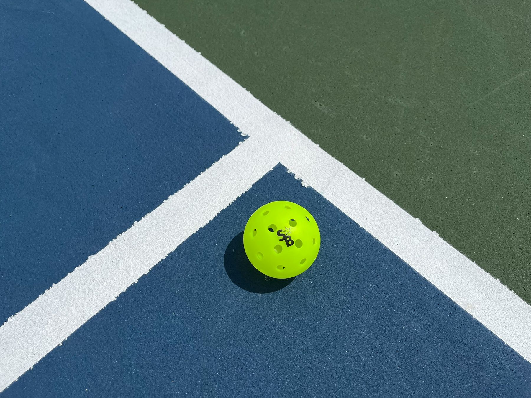 A pickleball on the line of a blue court